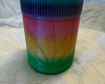 May include: A multi-colored glass jar with a green, yellow, pink, and blue glitter design. The jar has a leaf design on the front.