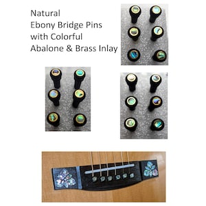 May include: Natural ebony bridge pins with colorful abalone and brass inlay. The set includes six black pins with circular iridescent shell centers and gold-toned metal rims. The text reads: Natural Ebony Bridge Pins with Colorful Abalone & Brass Inlay.