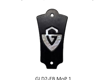 May include: A black ebony wood truss rod cover featuring a shield-shaped mother of pearl inlay with the letter G. The piece has two circular mounting holes and includes the text Ebony Wood w/Mother of Pearl Inlay and GLD2-EB MoP 1.