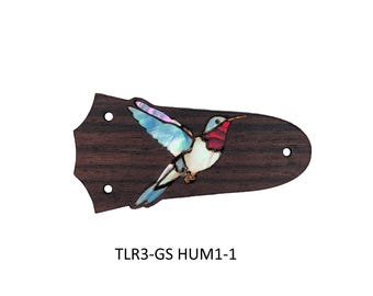 May include: A dark brown wooden guitar truss rod cover featuring an inlaid hummingbird design made of iridescent shell material with blue, white, and red accents. The piece has three pre-drilled mounting holes and the text TLR3-GS HUM1-1.
