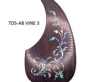 May include: A dark brown teardrop-shaped guitar pickguard featuring an iridescent abalone shell inlay in a vine pattern. The text TD5-AB VINE 3 is printed in black on the left side of the dark wood-grain textured surface of the guitar accessory.