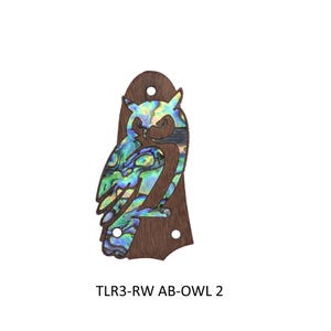 May include: A wooden guitar headstock overlay featuring an owl design. The owl is inlaid with iridescent abalone shell, showcasing a spectrum of blues, greens, and yellows. The overlay has a dark brown finish, with two small holes and the text "TLR3-RW AB-OWL 2".