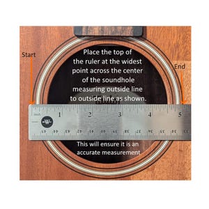 May include: A wooden guitar soundhole with a metal ruler placed across the center to measure the diameter. The text reads: Place the top of the ruler at the widest point across the center of the soundhole measuring outside line to outside line as shown. This will ensure it is an accurate measurement.