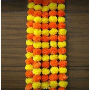 May include: A garland of artificial marigold flowers, alternating between yellow and orange. The garland is made of fabric and is perfect for decorating for a festival or special occasion.