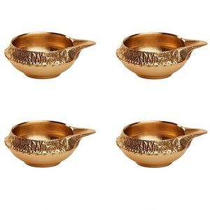 May include: Set of eight gold-colored brass diya oil lamps with intricate designs. Each diya has a small, round bowl and a curved spout.