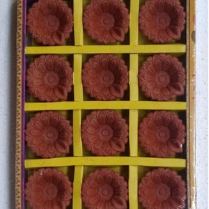 May include: A box of 12 terracotta diya lamps, each with a floral design. The diyas are arranged in a grid pattern and are ready for use.