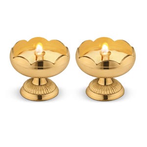 May include: Two gold metal oil lamps with a decorative scalloped edge and a round base. The lamps are lit with a small flame in the center of each.