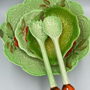Puede incluir: Un juego de servir ensalada de cerámica con una gran fuente verde en forma de lechuga, un cuenco más pequeño y dos cucharas de servir. Las cucharas tienen mangos verdes y extremos bulbosos de color naranja-rojizo. El juego está diseñado con texturas y detalles de hojas.