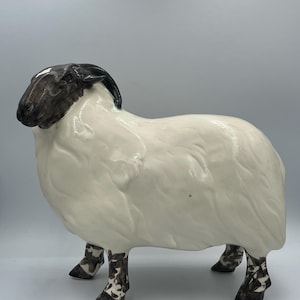 May include: A ceramic sheep ornament with a white body and a black head. The sheep has detailed features, including textured wool and patterned legs. This decorative item is a charming addition to any home.