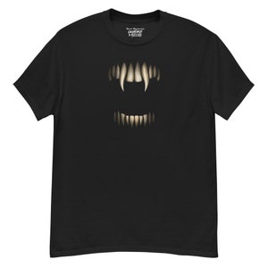 Può includere: T-shirt nera con un'illustrazione dettagliata dei denti di un mostro. Il design include zanne affilate e denti più piccoli, creando un aspetto minaccioso. La maglietta ha anche il testo "Creatures + Killers" in alto.
