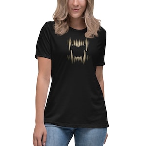 May include: Black t-shirt featuring a detailed graphic of sharp, menacing teeth. The teeth are a light beige color, contrasting against the dark background of the shirt. The design is centered on the front of the tee.