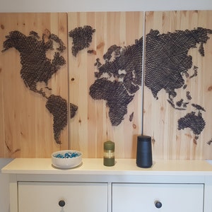May include: A three-panel wooden world map artwork. The continents are depicted with black string against a light wood backdrop. A white shelf below displays a bowl of blue stones, a green candle, and a black tumbler.