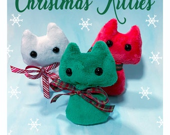 May include: Three plush cat toys in white, green, and red, each with large black eyes and a decorative ribbon. The toys are arranged on a light blue background with snowflakes and the text "Christmas Kitties".