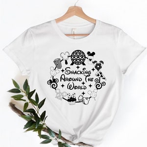 May include: White t-shirt with a black graphic design of a circle with various Disney snacks and the text "Snacking Around the World".