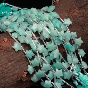 May include: A strand of teal green star-shaped gemstone beads strung on silver wire. The beads are faceted and have a natural, organic look. The strand is finished with a tassel on each end.