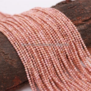 May include: A strand of pink gemstone beads, each bead is faceted and measures approximately 4mm in diameter. The beads are strung on a clear thread and are displayed on a piece of wood.