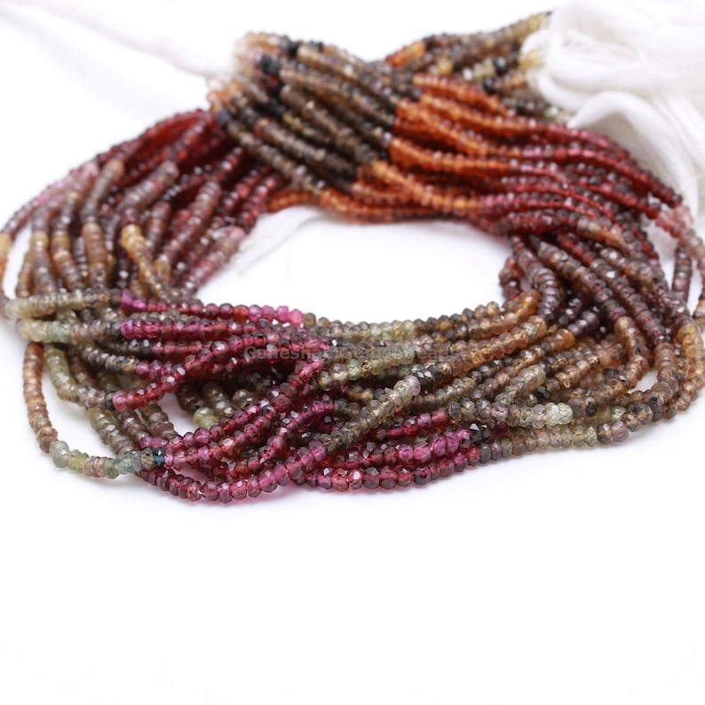 May include: A strand of faceted gemstone beads in shades of brown, orange, pink, and green. The beads are strung on a white cord and are arranged in a gradient pattern.