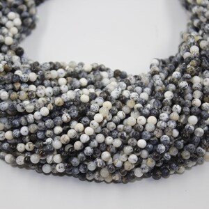 May include: A strand of black and white opal beads. The beads are round and have a speckled appearance.