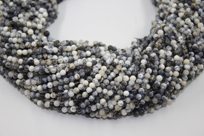 May include: A strand of black and white opal beads. The beads are round and have a speckled appearance.