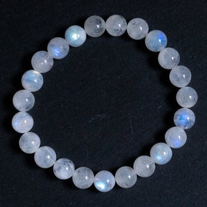 May include: A white moonstone bracelet with iridescent blue and white hues. The bracelet is made of round beads and is approximately 7 inches in length.