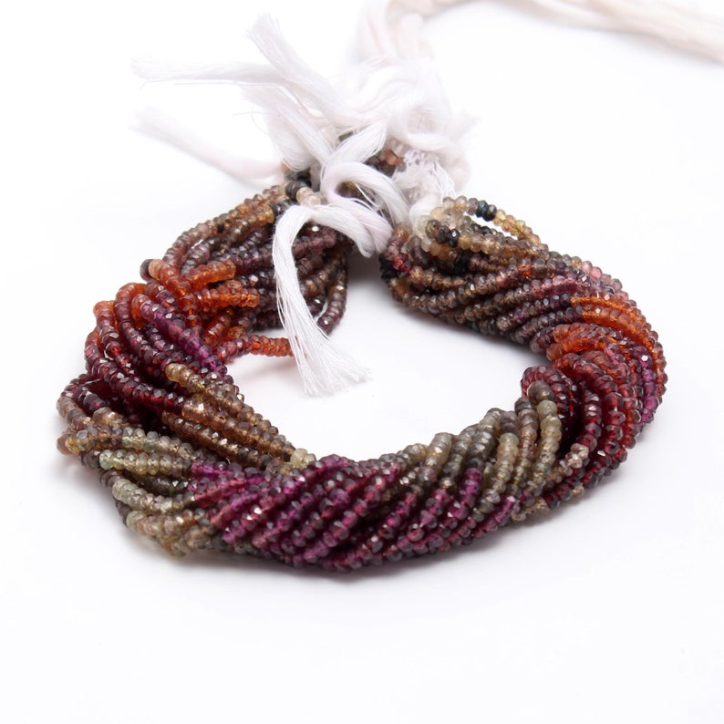 May include: A strand of faceted gemstone beads in shades of brown, orange, and pink. The beads are small and round, and they are strung on a white cord.
