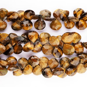 Könnte beinhalten: Stränge facettierter Tigeraugen-Edelsteinperlen. Die Perlen weisen warme Braun- und Goldtöne auf, mit einer polierten, reflektierenden Oberfläche. Die Perlen sind in Reihen vor einem weißen Hintergrund angeordnet.