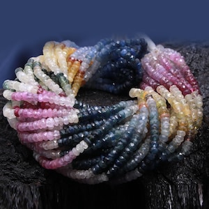 Könnte beinhalten: Eine Strähne aus facettierten Edelsteinperlen in verschiedenen Farben, darunter Blau, Rosa, Gelb und Weiß. Die Perlen sind kreisförmig angeordnet und bilden ein farbenfrohes und auffälliges Display.