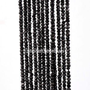 May include: A strand of black faceted gemstone beads. The beads are small and uniform in size, and they are strung on a clear thread. The beads are arranged in a straight line, and they are all facing the same direction.