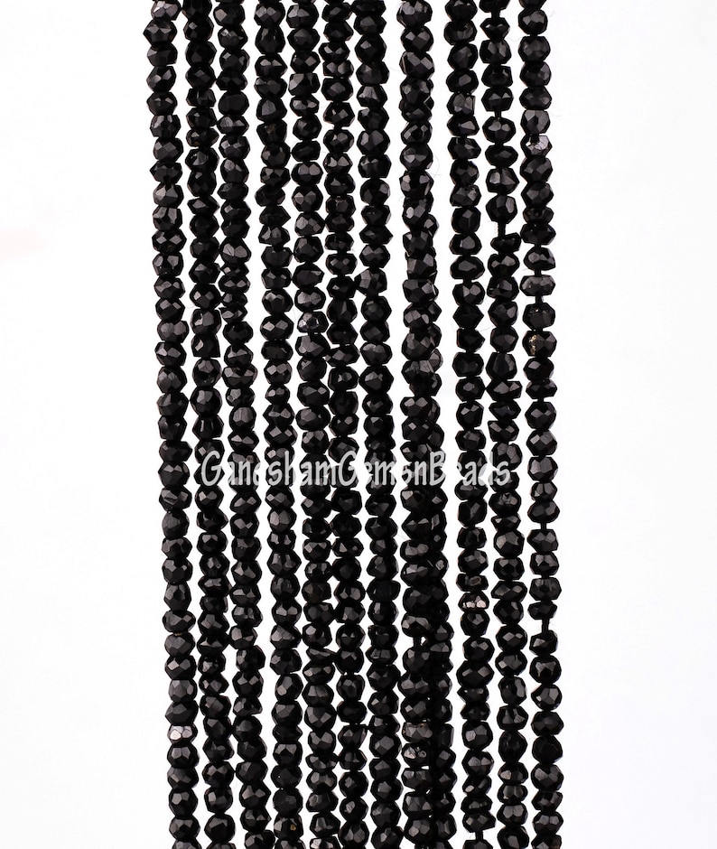May include: A strand of black faceted gemstone beads. The beads are small and uniform in size, and they are strung on a clear thread. The beads are arranged in a straight line, and they are all facing the same direction.