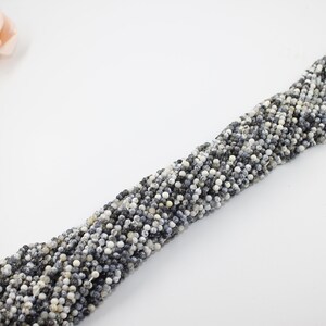 May include: A strand of white and gray speckled round beads. The beads are strung on a white thread.