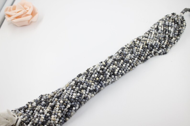 May include: A strand of white and gray speckled round beads. The beads are strung on a white thread.