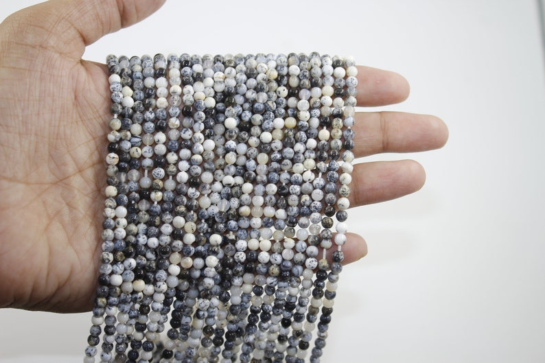 May include: A strand of white and black speckled round beads. The beads are approximately 4mm in diameter and are strung on a clear elastic cord.