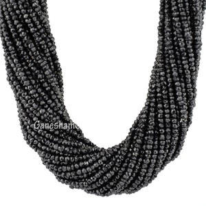 May include: A strand of black faceted gemstone beads. The beads are small and round, and they are strung together on a clear thread. The beads are arranged in a loose, flowing pattern.