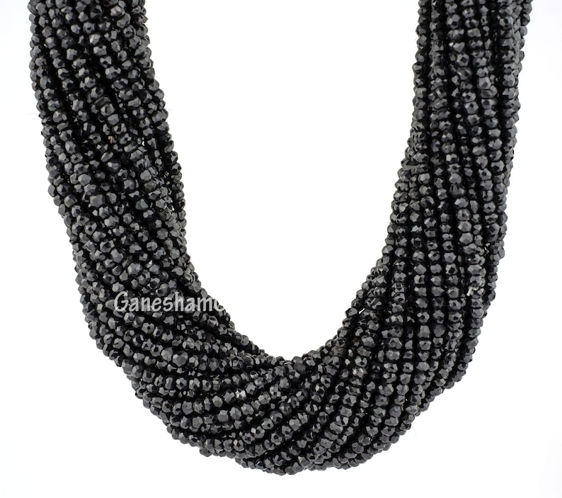 May include: A strand of black faceted gemstone beads. The beads are small and round, and they are strung together on a clear thread. The beads are arranged in a loose, flowing pattern.