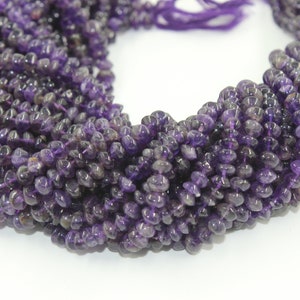 Könnte beinhalten: Eine Strähne aus violetten Amethyst-Edelsteinkugeln. Die Kugeln sind facettiert und haben eine glatte, polierte Oberfläche. Die Kugeln sind auf einem dünnen, durchsichtigen Faden aufgefädelt.