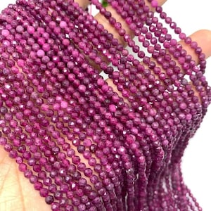 Könnte beinhalten: Eine Strähne aus rubinroten Edelsteinperlen, facettiert und rund, auf einem durchsichtigen Faden aufgereiht. Die Perlen sind klein und gleichmäßig in der Größe, was einen zarten und eleganten Look erzeugt.