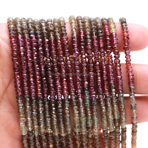 May include: A strand of faceted gemstone beads in shades of brown, green, and pink. The beads are small and uniform in size, and they are strung on a clear thread.