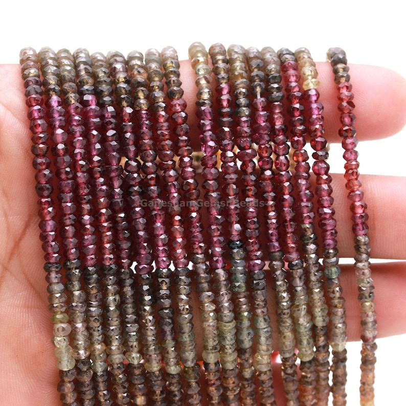 May include: A strand of faceted gemstone beads in shades of brown, green, and pink. The beads are small and uniform in size, and they are strung on a clear thread.
