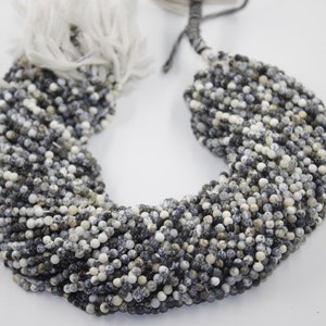 May include: A strand of small, round, speckled beads in shades of white, gray, and black. The beads are strung together on a white cord.