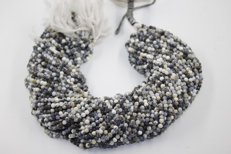 May include: A strand of small, round, speckled beads in shades of white, gray, and black. The beads are strung together on a white cord.