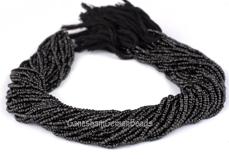 May include: A strand of black faceted glass beads. The beads are small and uniform in size. The strand is coiled into a circle.