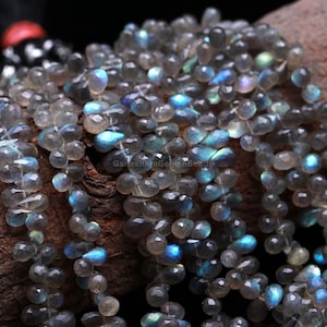 Può includere: Un filo di perline di labradorite sfaccettata grigia con bagliori iridescenti blu e verdi. Le perline sono a forma di goccia e misurano circa 6 mm.