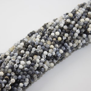 May include: A strand of black and white round gemstone beads. The beads are made of natural stone and have a speckled pattern.