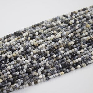 May include: A strand of black and white speckled round gemstone beads. The beads are approximately 4mm in diameter and have a natural, polished finish.