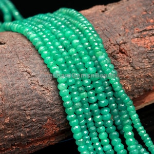 Peut inclure: Un brin de perles de pierres précieuses vertes, facettées et rondes, disposées en rangées sur une surface en bois.