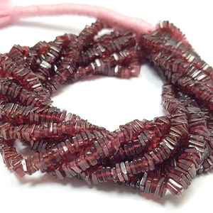 Puede incluir: Una hebra de cuentas de piedras preciosas de color rojo oscuro, cada cuenta es un prisma rectangular con una forma ligeramente irregular. Las cuentas están enhebradas en un cordón delgado.