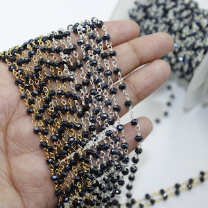 May include: A strand of black faceted beads strung on a silver and gold chain. The chain is made of small, delicate links. The beads are evenly spaced and have a shiny finish.