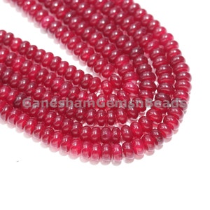 Könnte beinhalten: Eine Strähne tief roter Edelsteinperlen. Die Perlen sind rund und glatt, mit einem glänzenden Finish.