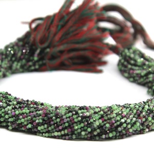 Könnte beinhalten: Eine Strähne aus grünen, rosa und schwarzen Edelsteinperlen. Die Perlen sind facettiert und haben eine glänzende Oberfläche. Die Strähne ist etwa 45 cm lang.