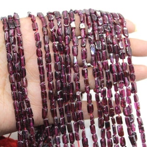 Puede incluir: Una hebra de cuentas de granate rojo oscuro, cada cuenta está facetada y tiene una forma rectangular. Las cuentas están enhebradas en un alambre delgado y tienen aproximadamente 6 mm de tamaño.